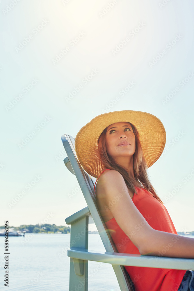 Fototapeta premium This is how I start everyday. a cheerful young woman wearing a hat while being seated on a chair next to a lake outside in the sun.