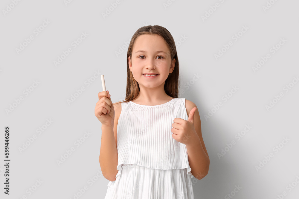 Little girl with chalk piece showing thumb-up on light background. Children's Day celebration Little girl with chalk piece showing thumb-up on light background. Children's Day celebration