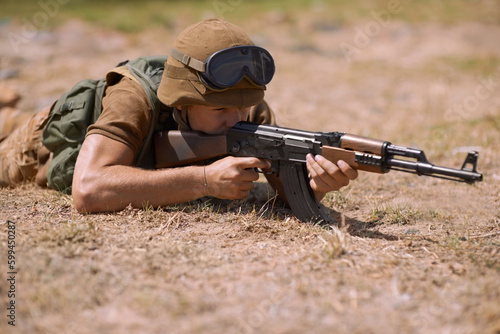 Stalking the enemy. A young soldier aiming with his rifle while lying on the ground.