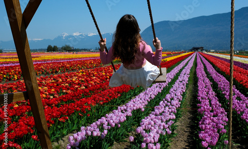 Young attractive blond woman in white summer dress swings on chain swing in coloful tulip fields. space for text ad travel vacation relaxation slow motion video Chilliwack. British Columbia. Canada photo