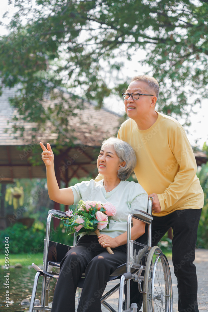 Senior couple and disabled wife in wheelchair with flower bouquet to watching nature view in park