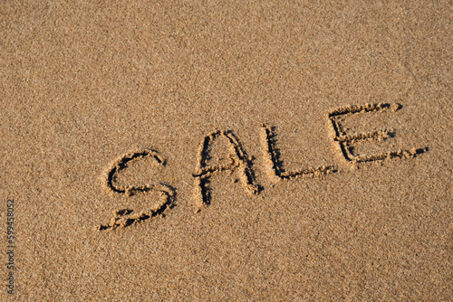 Text SALE handwritten in sand surface. Concept of promotion Black Friday Blue ocean wave washing away message at the beach. Summer holidays beach writing vacation concept