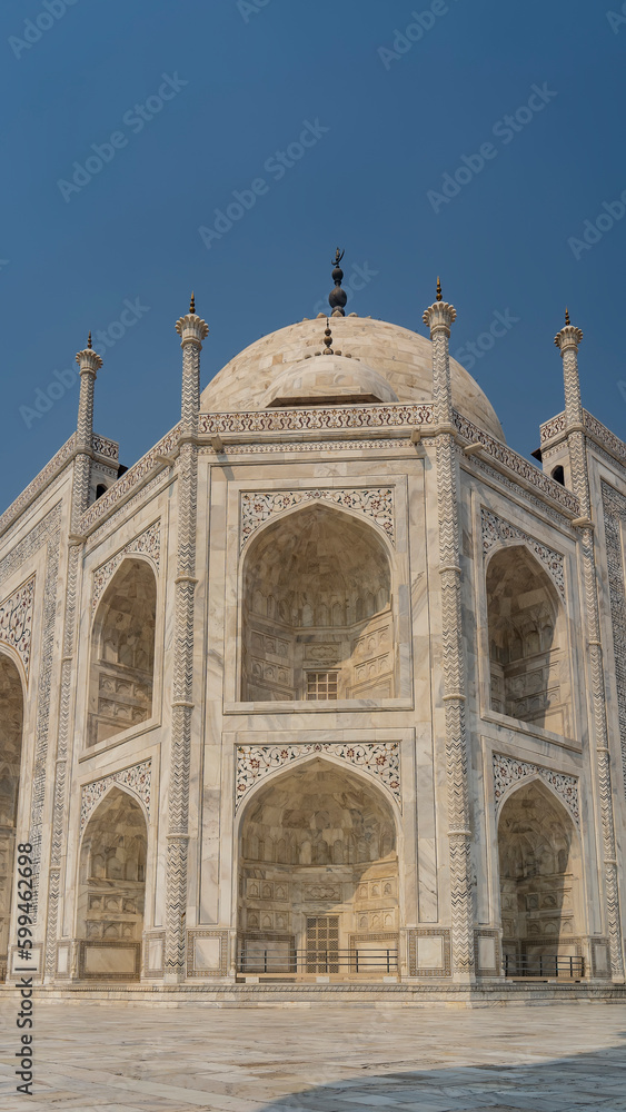 Beautiful white marble Taj Mahal against the blue sky. The symmetrical mausoleum with arches, domes, spires is decorated with ornaments, inlays of precious stones. India. Agra