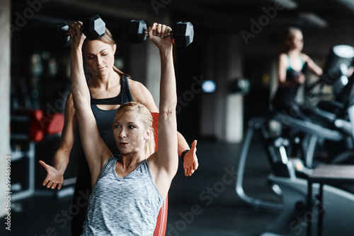 Just take it nice and easy. a mature woman lifting weights with a female instructor at the gym.