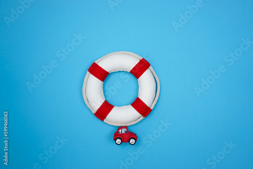 The concept of summer recreation on water spaces. A red retro toy car is carrying a red and white lifebuoy.