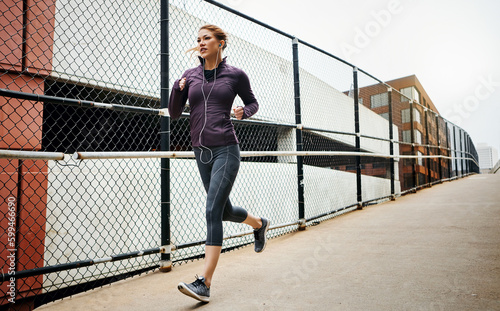One stride at a time. Full length shot of an attractive young woman listening to music while running through the city.