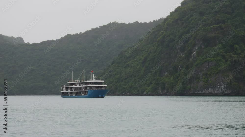 Blue Cruise Ship Passing On Mountains background In Ha Long Bay, Northeast Vietnam. Slow Motion Blue Cruise Ship Passing On Mountains background In Ha Long Bay, Northeast Vietnam. Slow Motion