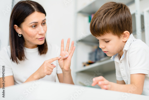 Beautiful woman speech therapist teaches boy the correct pronunciation of words and sounds in the office