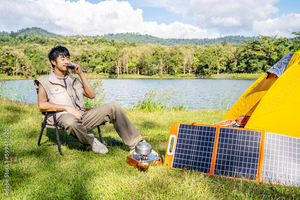 Fototapeta premium Young Asian traveling man relax and enjoy outdoor lifestyle camping in forest mountain on summer holiday travel vacation. Attractive male drinking coffee while enjoys drink among green trees