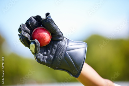 Cricket, ball and hand with a wicket keeper making a catch during a sports game outdoor on a pitch. Fitness, glove and caught with a sport player playing a competitive match outside during summer photo