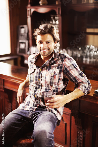 Portrait, smile and man with whiskey in pub sitting by counter alone. Alcohol, happiness and male person in bar for drinking liquor, beverage or drink in tavern, relaxing and enjoying time alone.