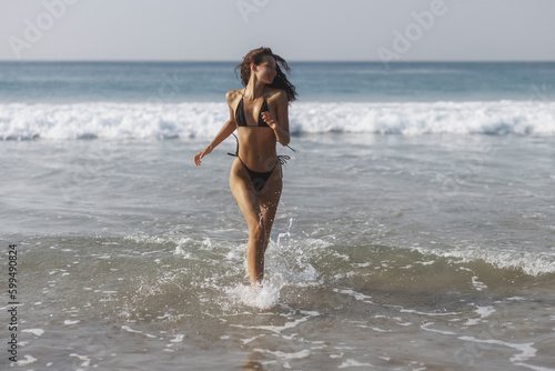 Happy bikini beach vacation woman running to ocean splashing water in