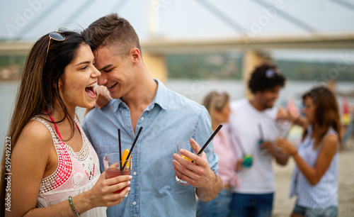 Happy young people, friends having fun on the beach and drinking cocktails together.