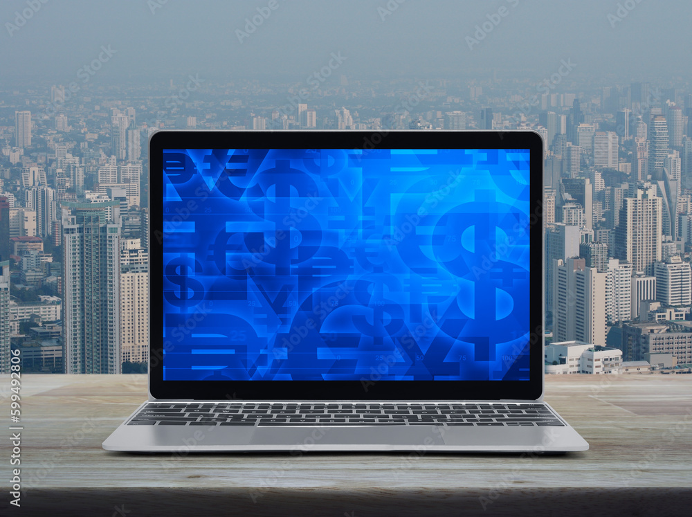 Financial currency symbol on modern laptop computer screen on wooden table over city tower and skyscraper Financial currency symbol on modern laptop computer screen on wooden table over city tower and skyscraper