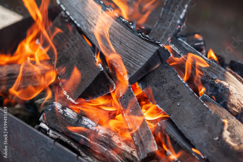 The firewood in the grill burns with a bright orange flame. Preparation for cooking meat on the grill in nature. Fire flames and smoke 