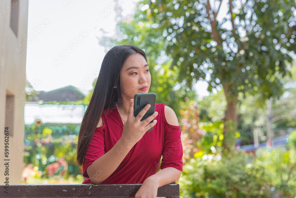 A white Asian Filipino girl wearing a long red dress leaning on a rail staring at a distance with a serious face while holding her phone up. Plants and trees are in the background. A white Asian Filipino girl wearing a long red dress leaning on a rail staring at a distance with a serious face while holding her phone up. Plants and trees are in the background.