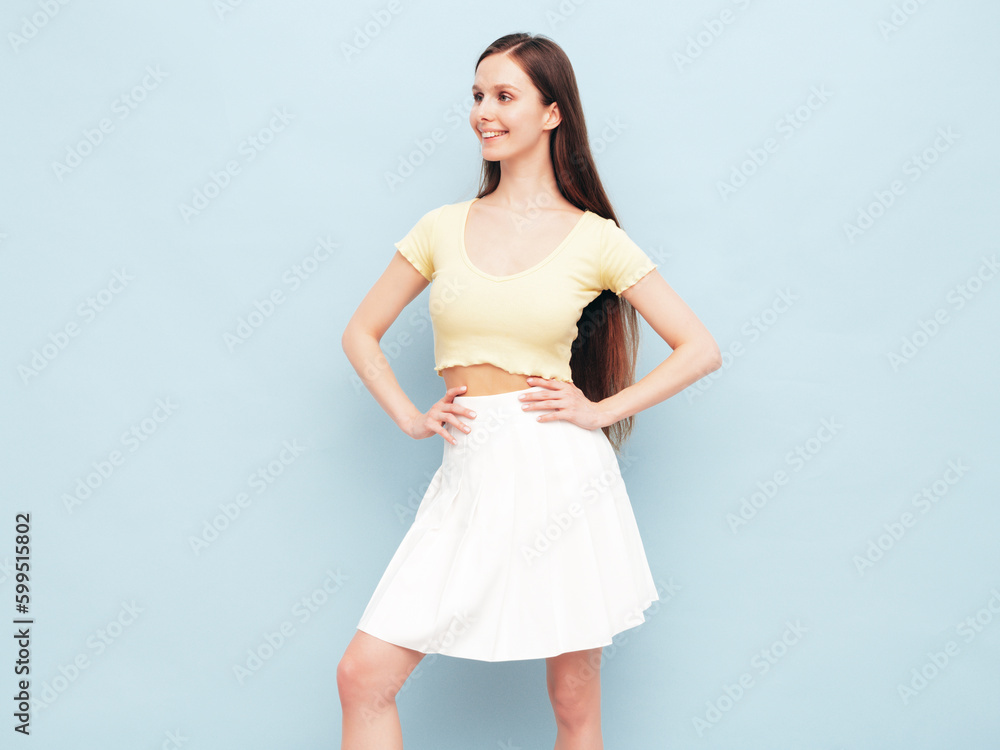 Fototapeta premium Image portrait of optimistic woman in yellow t-shirt and white skirt. Carefree stylish model with long hair. Smiling female posing in studio. Isolated. Looks delightful and cute. Slim