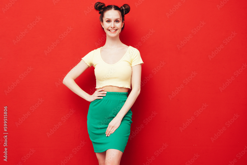 Young beautiful smiling female in trendy summer yellow t-shirt and green skirt. Carefree woman with two horns hairstyle posing near red wall in studio. Positive model having fun. Cheerful and happy Young beautiful smiling female in trendy summer yellow t-shirt and green skirt. Carefree woman with two horns hairstyle posing near red wall in studio. Positive model having fun. Cheerful and happy