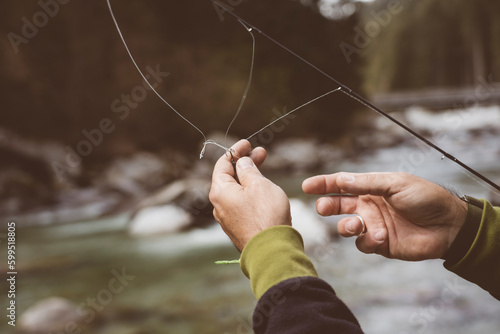 Mani di pescatore che cercano di snodare il filo da pesca con attaccato un'esca artificiale per la pesca allo spinning. photo