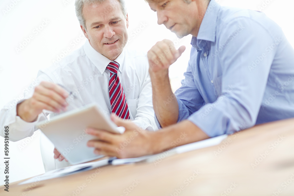 Interesting business developments. Two male colleagues in a meeting with a tablet discussing business strategy. Interesting business developments. Two male colleagues in a meeting with a tablet discussing business strategy.