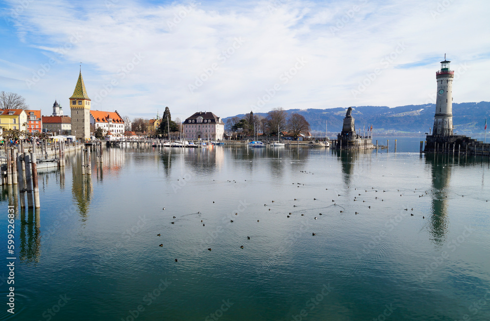 sunlit harbour and beacon of Lindau on tranquil lake Constance (lake Bodensee) with the Alps in the background on a sunny evening in winter (Lindau, Germany)	