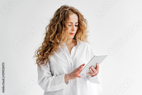 A young red-haired female student uses a tablet, taps on the screen.