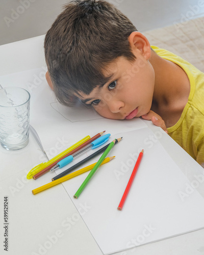 The boy is tired of studying. The child got tired and lay down on the textbook. The boy is engaged in creativity and thinks what to draw, The boy is looking for an idea for drawing. Child at the table