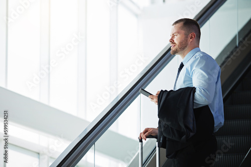 Taking his business global. a businessman traveling down an escalator in an airport.