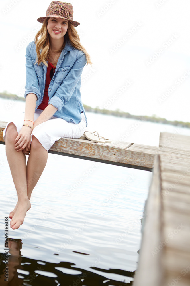 Peaceful moments by the lake. A happy young woman sitting on a jetty next to a lake.