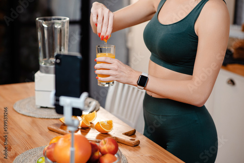 Cropped view of the fitness blogger preparing orange juice while recording video on smartphone