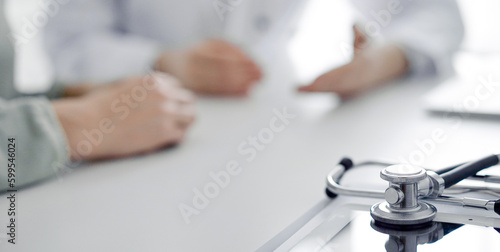 Doctor and patient sitting at the desk in clinic office. The focus is on female physician's hands using tablet computer, close up. Perfect medical service and medicine concept