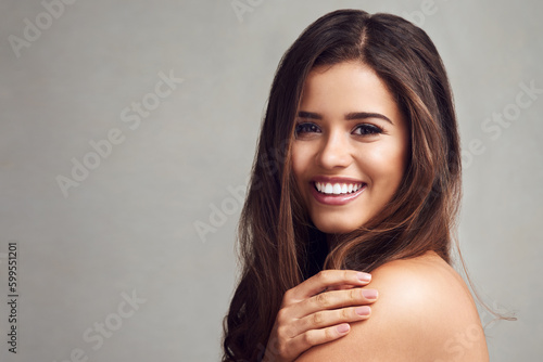 Soft to the touch is how I like my skin. Studio shot of a young beautiful woman with long gorgeous hair posing against a grey background. photo