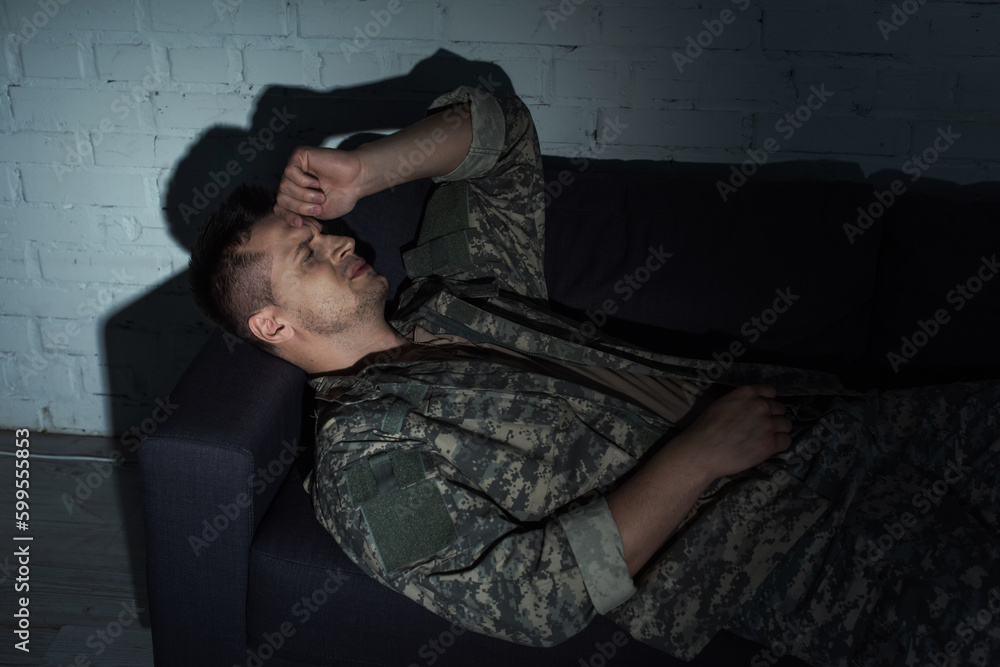 Obraz premium Depressed military man in uniform suffering from post traumatic stress disorder while lying on couch.