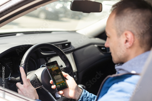 Close up cropped shot of man hand holding mobile phone with bookmaker;s website on its screen. Male gambler betting online using mobile application white sitting in a car.