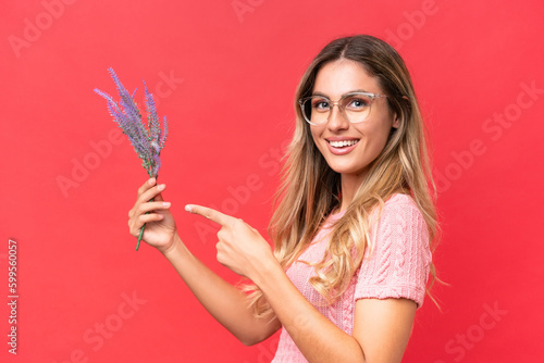 Young pretty Uruguayan woman holding lavender isolated on red background and pointing it