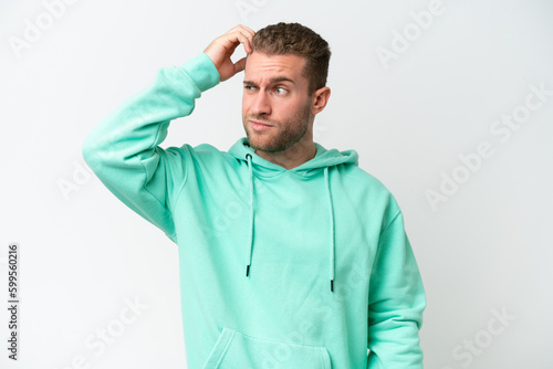 Young handsome caucasian man isolated on white background having doubts while scratching head © luismolinero