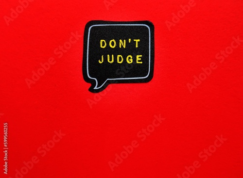 Speech bubble stick on red copy space background with text DON'T JUDGE, concept of  judging less, accept more, avoid judging someone else mistakes  to avoid realize our own. photo