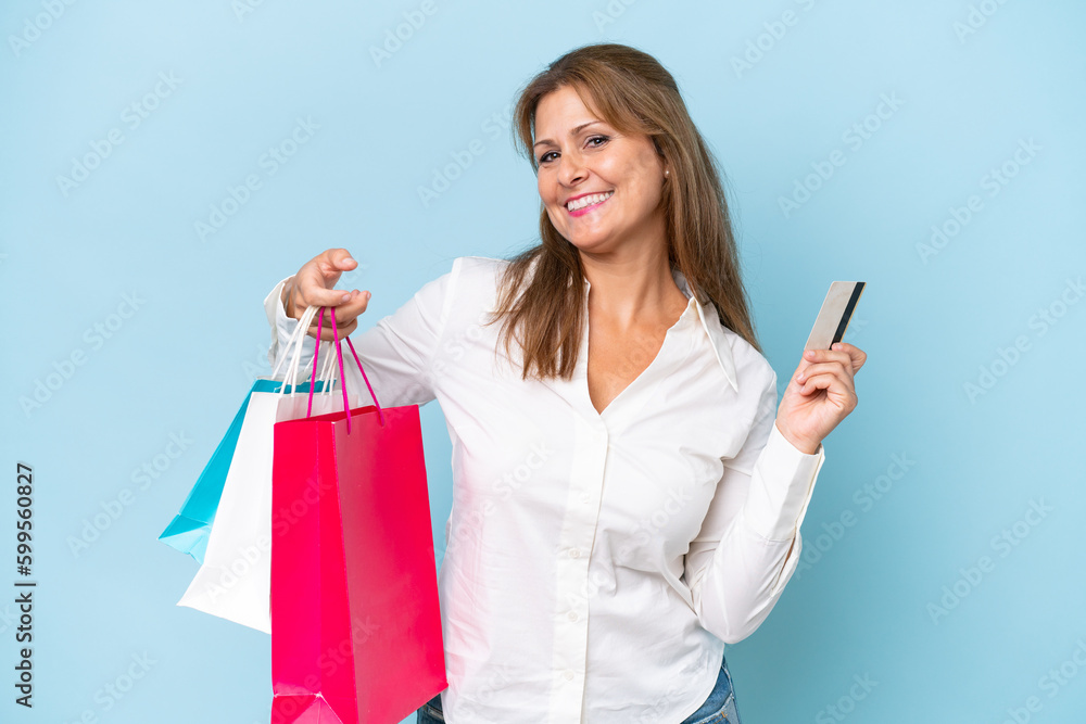 Middle-aged caucasian woman isolated on blue background holding shopping bags and a credit card Middle-aged caucasian woman isolated on blue background holding shopping bags and a credit card