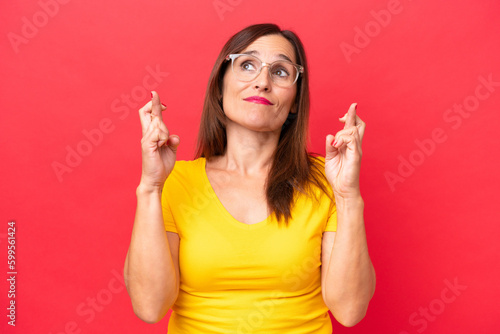 Middle-aged caucasian woman isolated on red background with fingers crossing and wishing the best