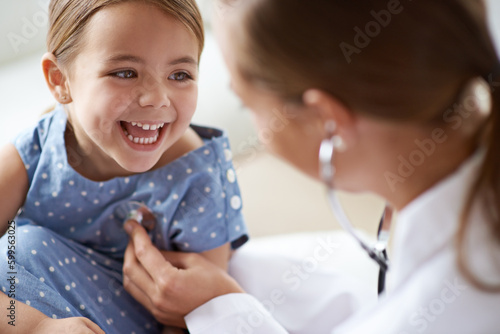 Happy child, girl and stethoscope of doctor for medical consulting, healthy lungs and listening to heartbeat. Face of laughing kid, pediatrician and chest assessment for healthcare analysis in clinic photo