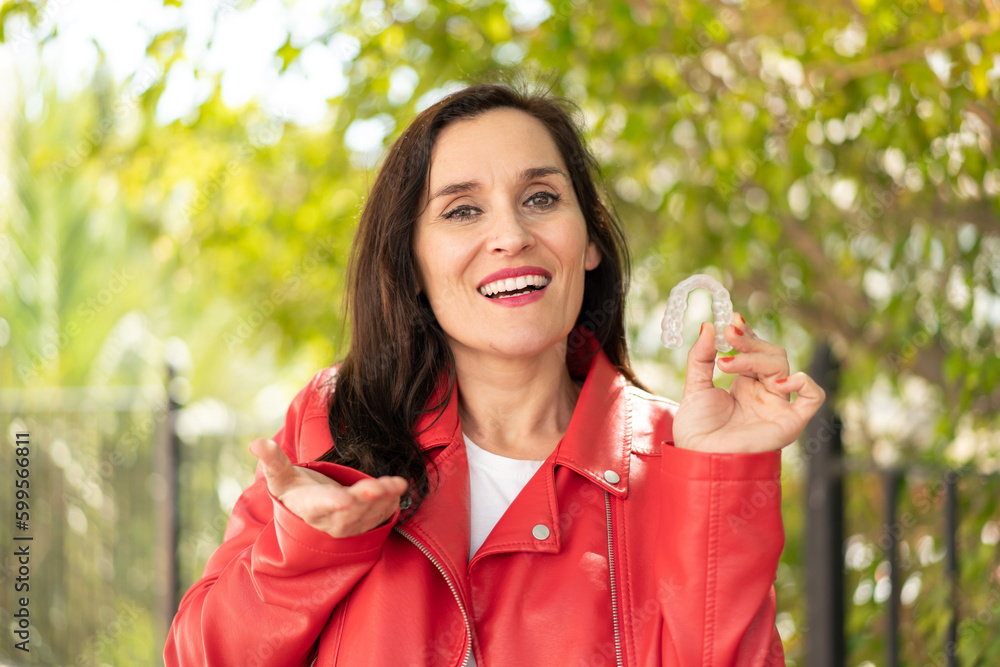 Middle aged woman holding invisible braces at outdoors with shocked facial expression Middle aged woman holding invisible braces at outdoors with shocked facial expression