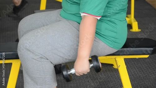 trainer teaching fat woman working hard in the gym lifting dumbbell