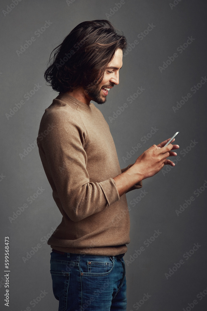 Fototapeta premium Now thats a meme worth sharing. Studio shot of a handsome young man using a mobile phone against a gray background.