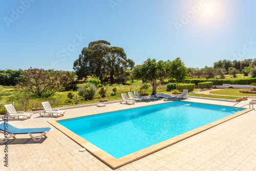 Private swimming pool with sun loungers and garden around. Sunny day. © sergojpg