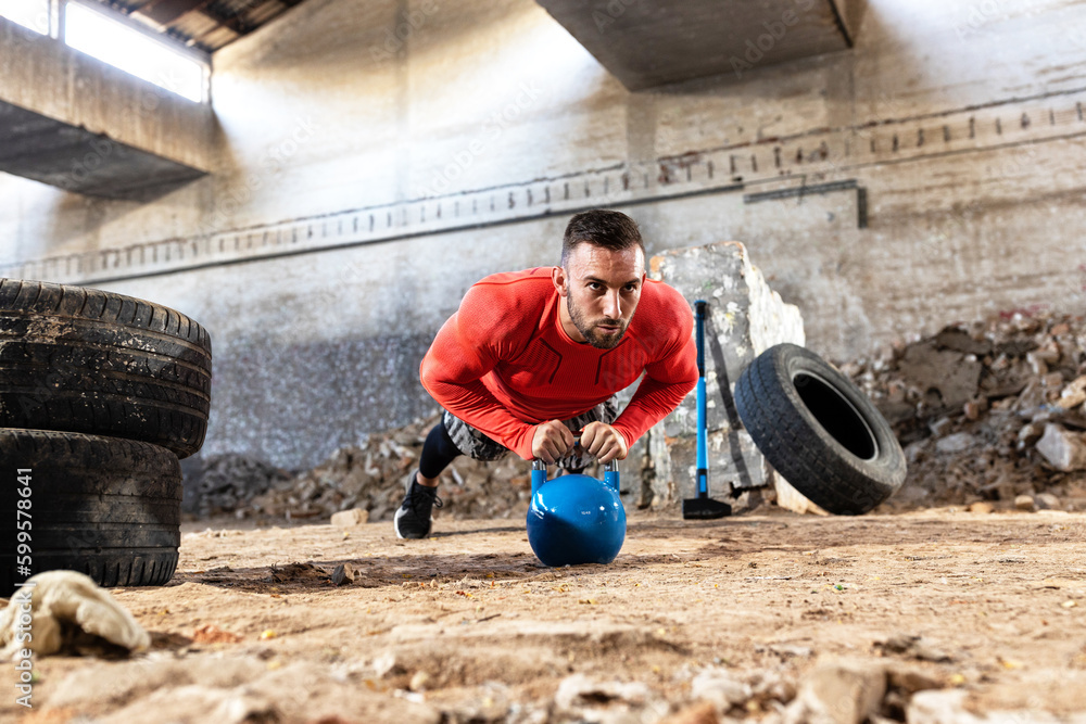 Muscular athlete doing push up on a kettlebell, increasing the range and motion of the pectoral muscle, working out a solid progression towards greater physique and stamina, closed factory-brickyard Muscular athlete doing push up on a kettlebell, increasing the range and motion of the pectoral muscle, working out a solid progression towards greater physique and stamina, closed factory-brickyard