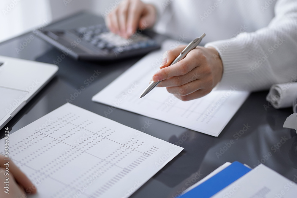 Woman accountant using a calculator and laptop computer while counting taxes for a client. Business audit and finance concepts Woman accountant using a calculator and laptop computer while counting taxes for a client. Business audit and finance concepts