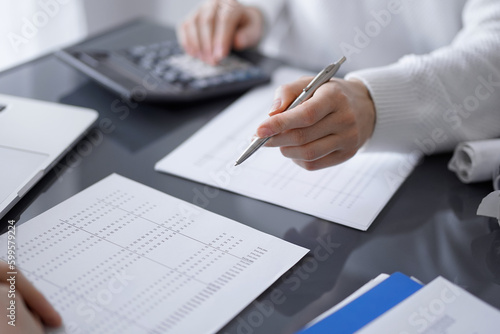 Woman accountant using a calculator and laptop computer while counting taxes for a client. Business audit and finance concepts