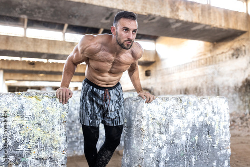 Ripped man with six pack training on huge rock-concrete cubes, fitness shape, chest exercises concept, old abandoned factory, industrial complex background