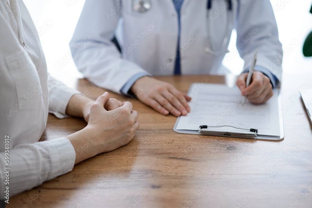 Doctor and patient discussing something while sitting near each other at the wooden desk in clinic. Medicine concept Doctor and patient discussing something while sitting near each other at the wooden desk in clinic. Medicine concept