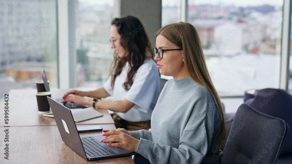 Positive young female colleagues work at laptops in the office. Calm working atmosphere. Positive young female colleagues work at laptops in the office. Calm working atmosphere.